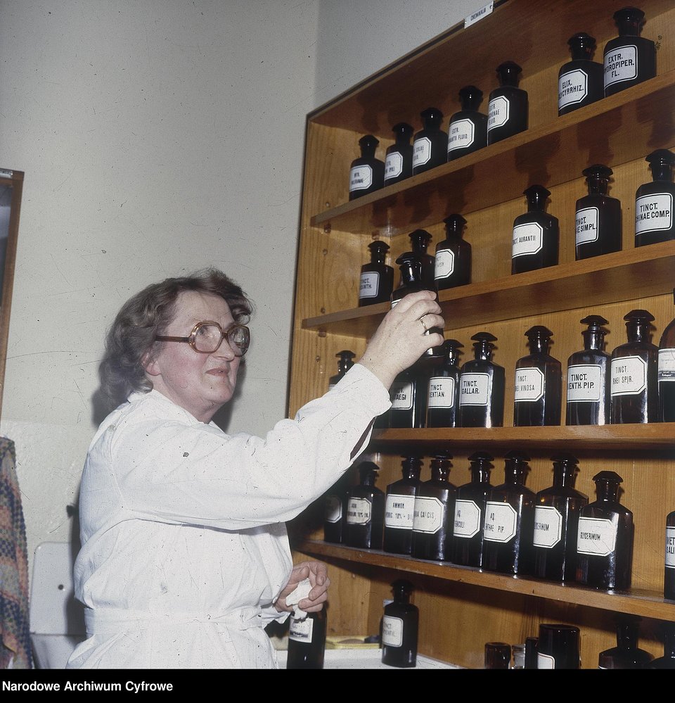 Krystyna Kordzik z Józefowa, farmaceutka pracująca w aptece w Międzylesiu, stoi przy regale z odczynnikami chemicznymi do sporządzania leków recepturowych, 1980 r.
